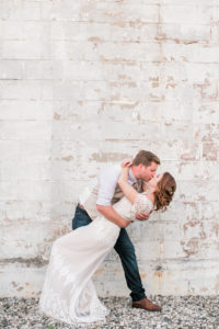 dip kiss bride and groom white brick wall