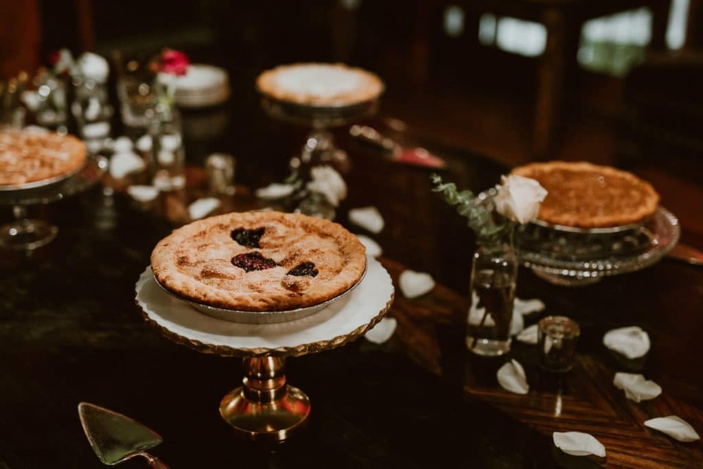 Dessert table with pies on cake stands with small bud vases with greenery