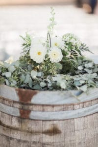 White flowers with greenery on vintage wine barrel for barn wedding