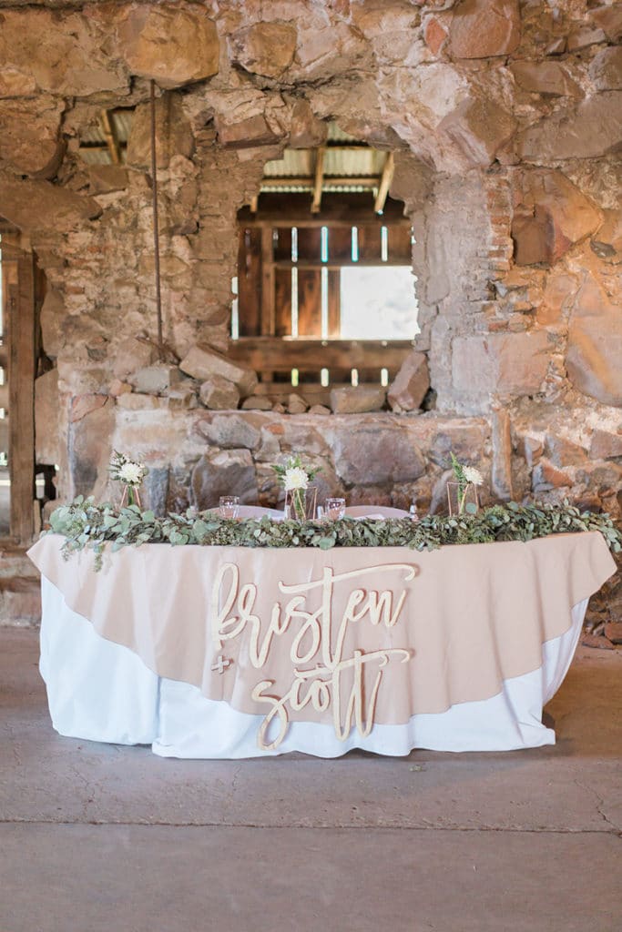 Sweetheart table inside old barn with green garland and wooden laser cutouts of bride and groom names