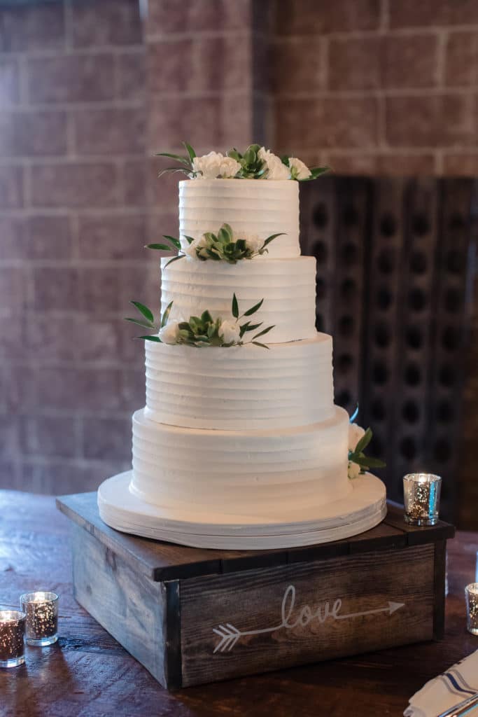 4 tiered white wedding cake with white flowers and greenery