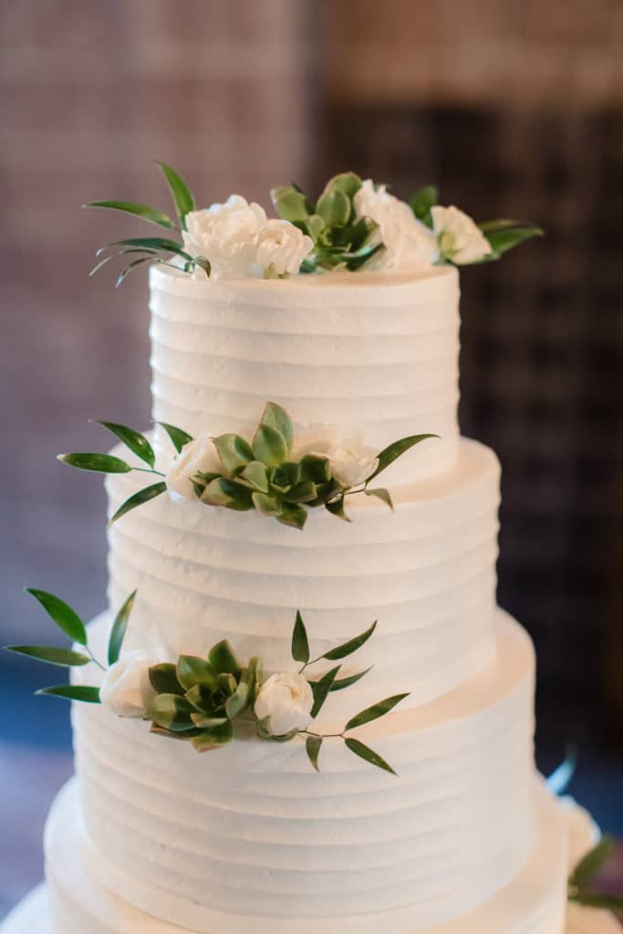 4 tiered white wedding cake with white flowers and greenery