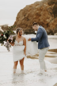 Bride laughing as wave gets bride and groom wet during elopement in Laguna Beach