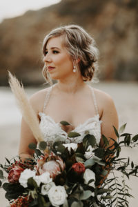 Bride with loose updo holding moody, wild bouquet in Laguna Beach