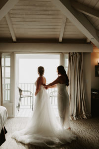 Maid of Honor helping bride get into dress for Laguna Beach elopement with ocean view