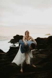 Bride getting piggy back ride while groom climbing rocks and laughing after elopement in Laguna Beach