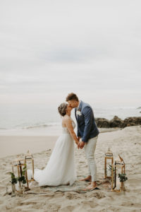 Bride and groom kiss on the beach with lanterns and boho run in Laguna Beach California