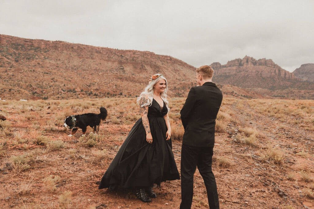 Tattooed Bride and groom in all black in desert at Zion Under Canvas. First look with the desert behind them before their epic glamping wedding,