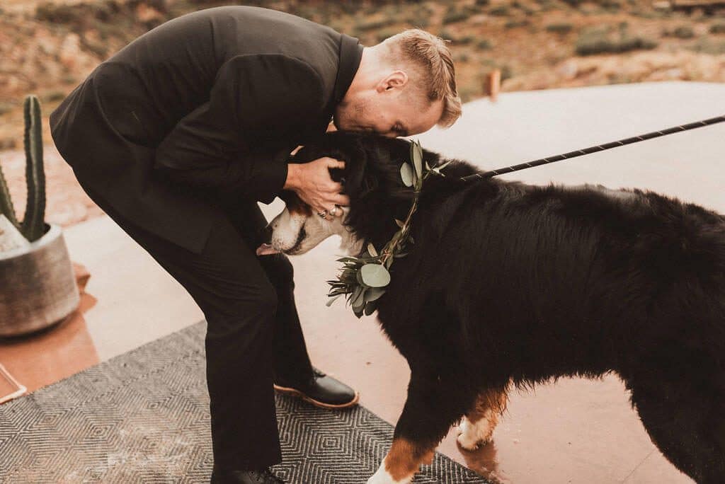 Groom in all black kisses his dog as he walks down the aisle to greet him
