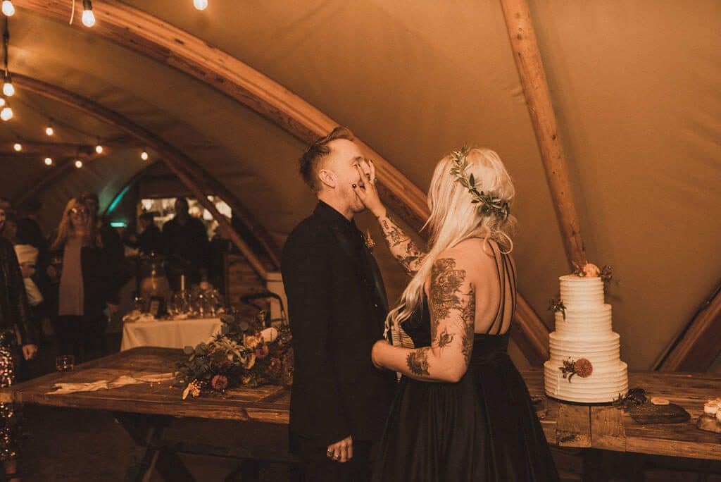 Tattooed bride in black wedding dress smashes cake into groom's face