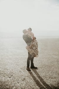 A bride and groom kiss each other during a surprise rain shower in the desert.