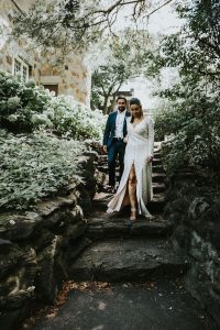 bride in slit dress walks down steps with groom in navy suit