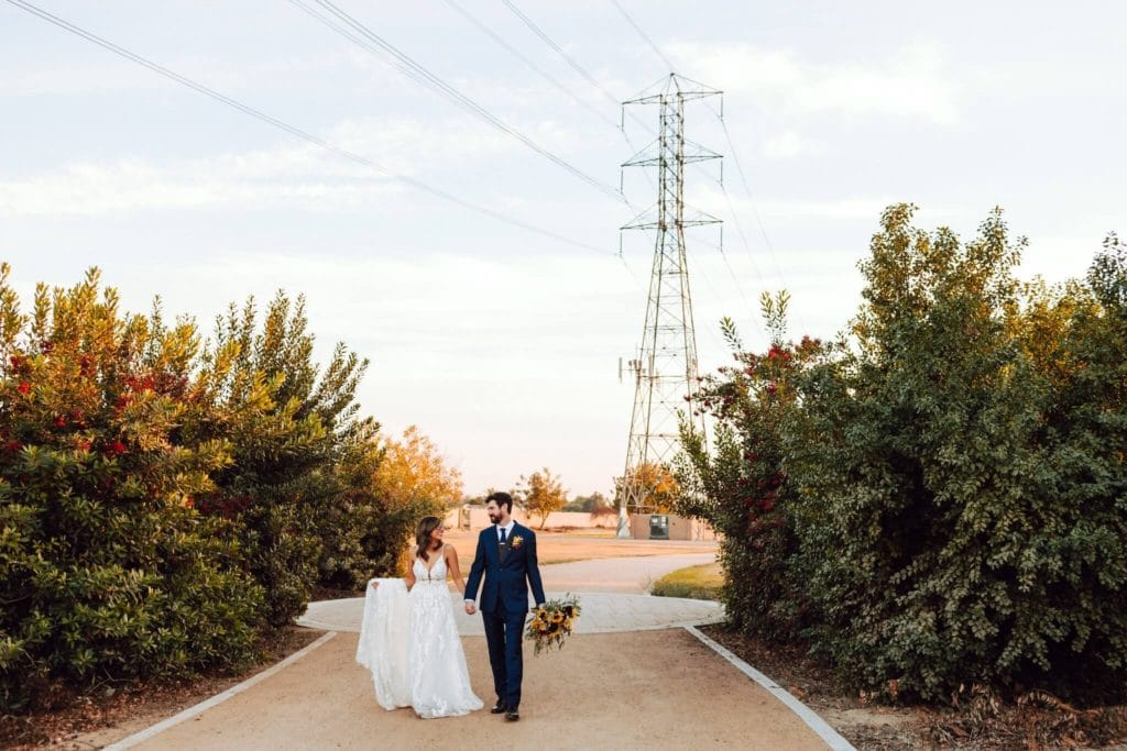 Bride and groom walking outside while holding hands and smiling