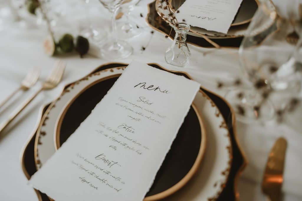 Layered black, white, and gold place setting with raw edge menu