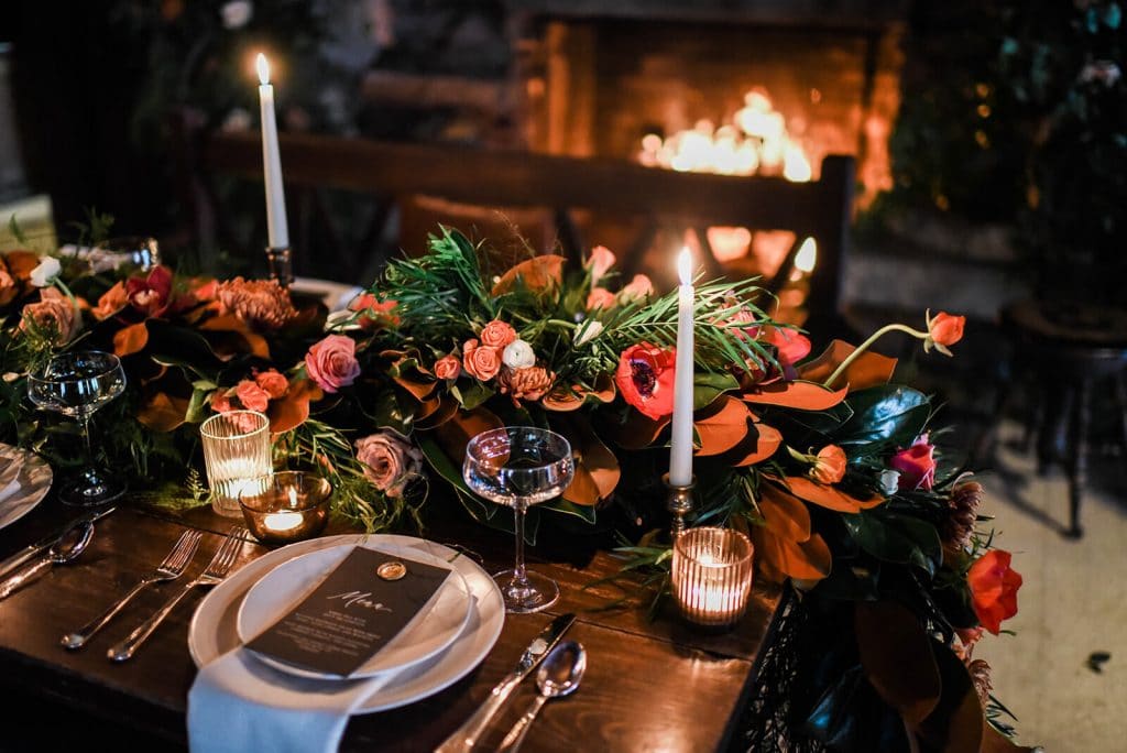 Indoor winter wedding table with candles, colorful florals and fireplace